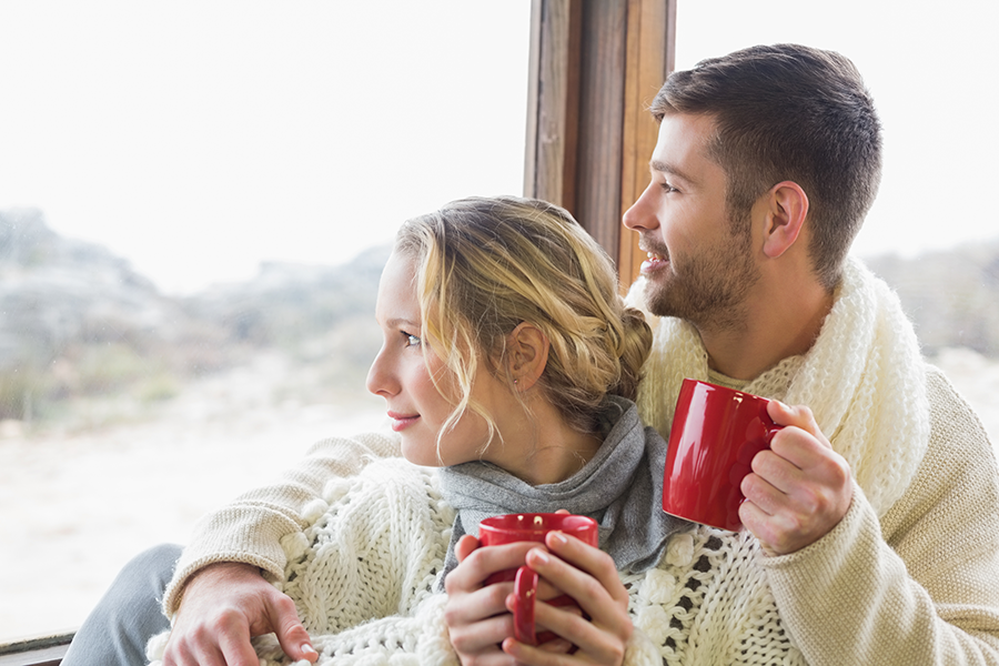 Couple snug and comfortable within home, sipping warm drinks.